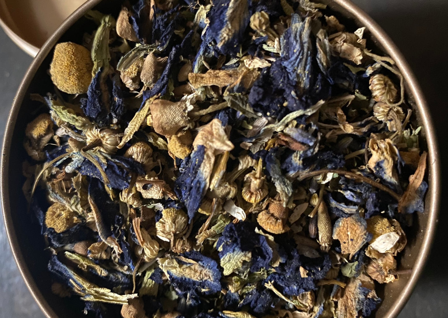 Blend of yellow chamomile flower with touches of blue flowers inside of a gold can